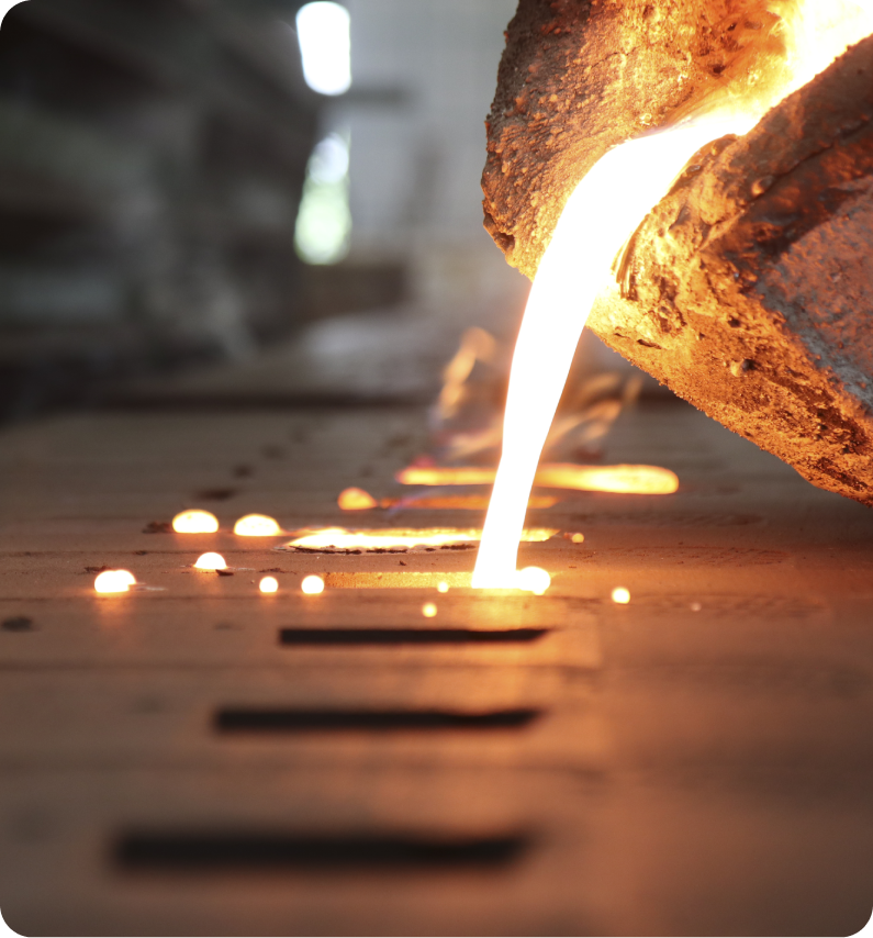 Molten metal being poured from a large container into molds on a casting floor.