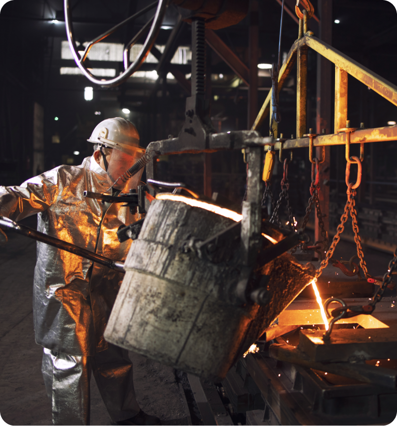 Worker in protective gear pours molten metal into a mold in an industrial foundry setting.