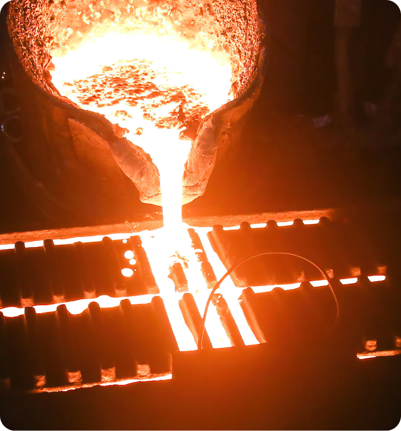 Molten metal pours from a large crucible into a mold, glowing brightly in a foundry setting.
